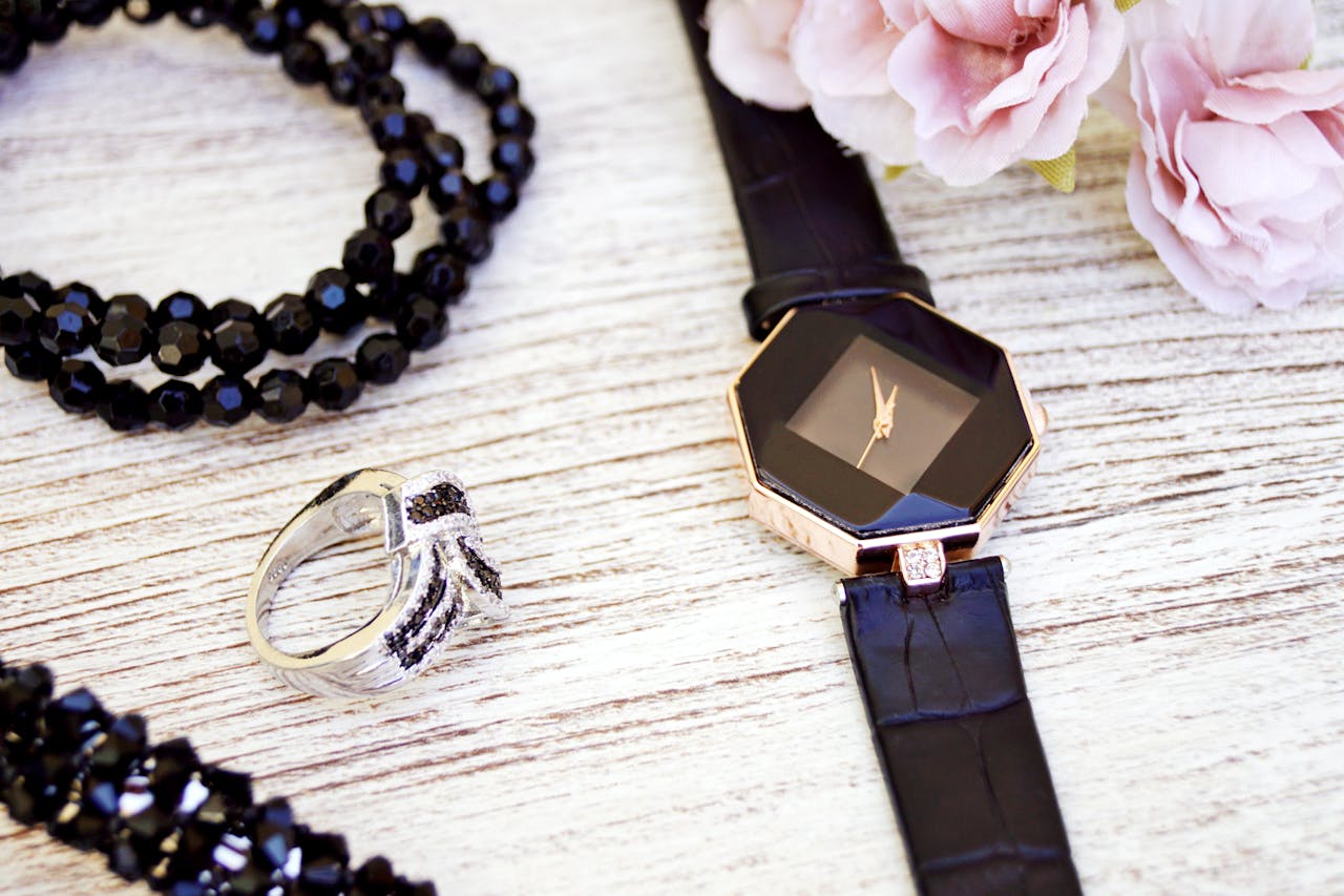 about-02 Close-up of luxurious black jewelry and watch with pink flowers on a wooden surface.