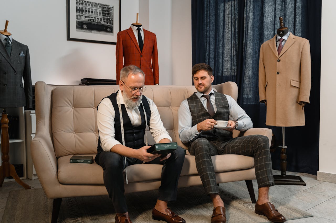 services-03 Two well-dressed men enjoying tea in an elegant tailoring workshop.